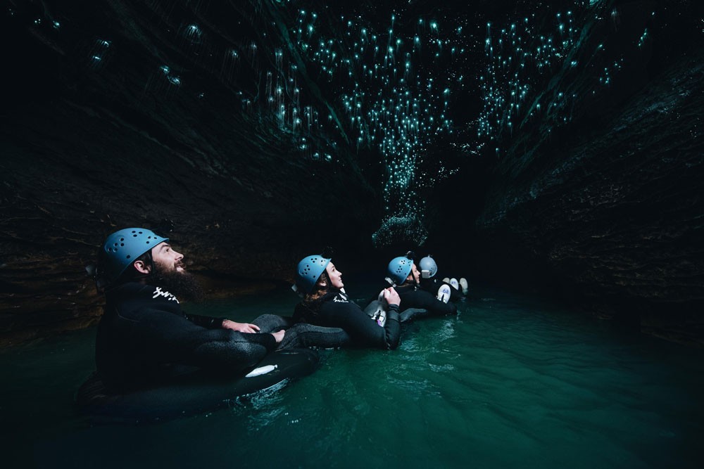 grupo de personas andando en las cuevas de Waitomo con una linterna y cascos de seguridad en la cabeza